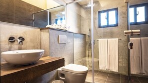 Uma casa de banho moderna com uma grande lavatório suspenso, uma sanita, um chuveiro com parede de vidro e um porta-toalhas.