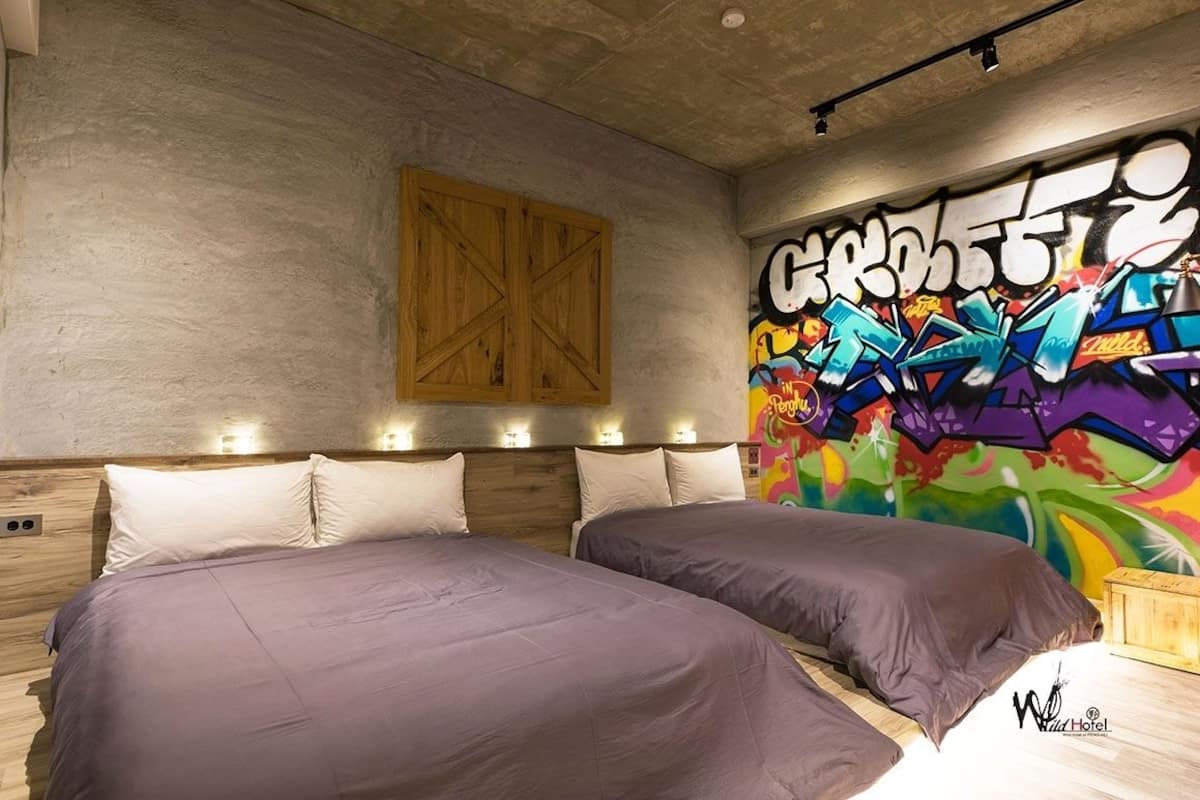 A room with two beds, a wooden headboard, a graffiti wall, and a wooden chest of drawers.