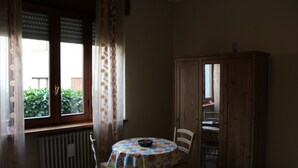 A room with a round table, a chair, a cabinet, and a window with curtains. - B&B Milano Malpensa 1 (Castano Primo)