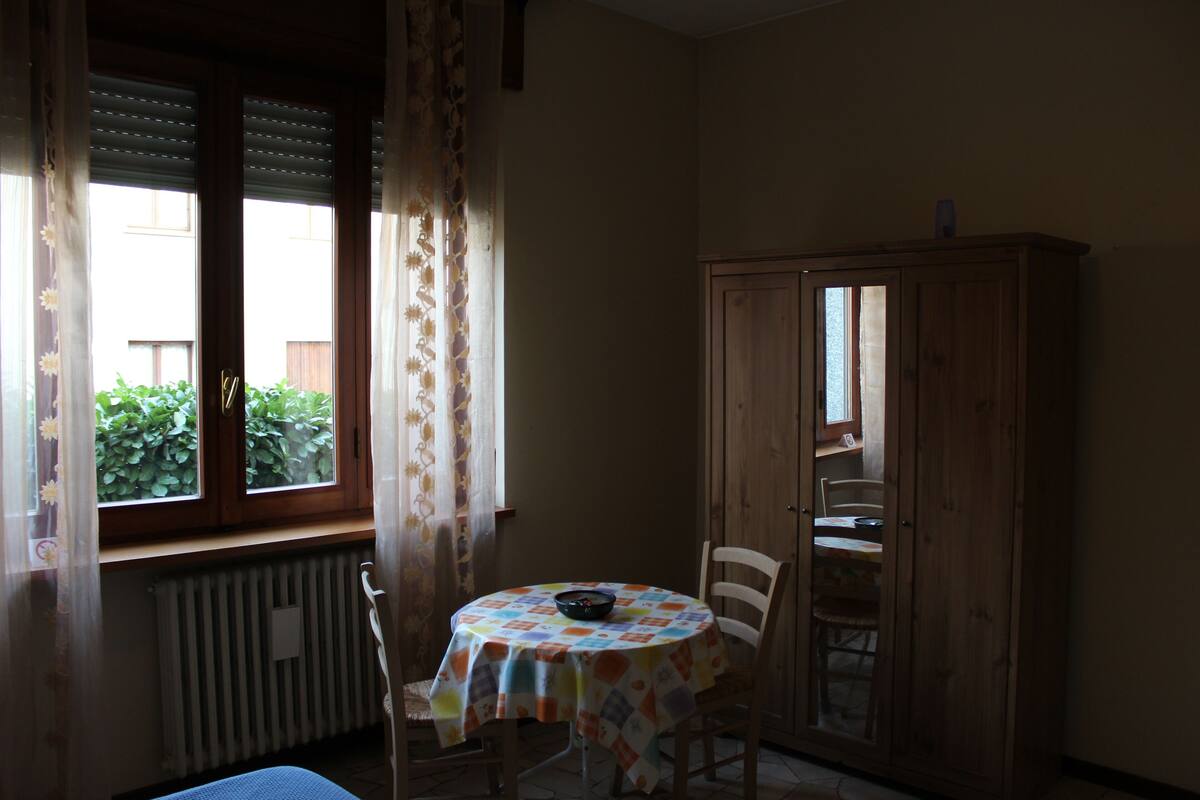 Ein Zimmer mit einem runden Tisch, einem Stuhl, einem Schrank und einem Vorhangfenster.