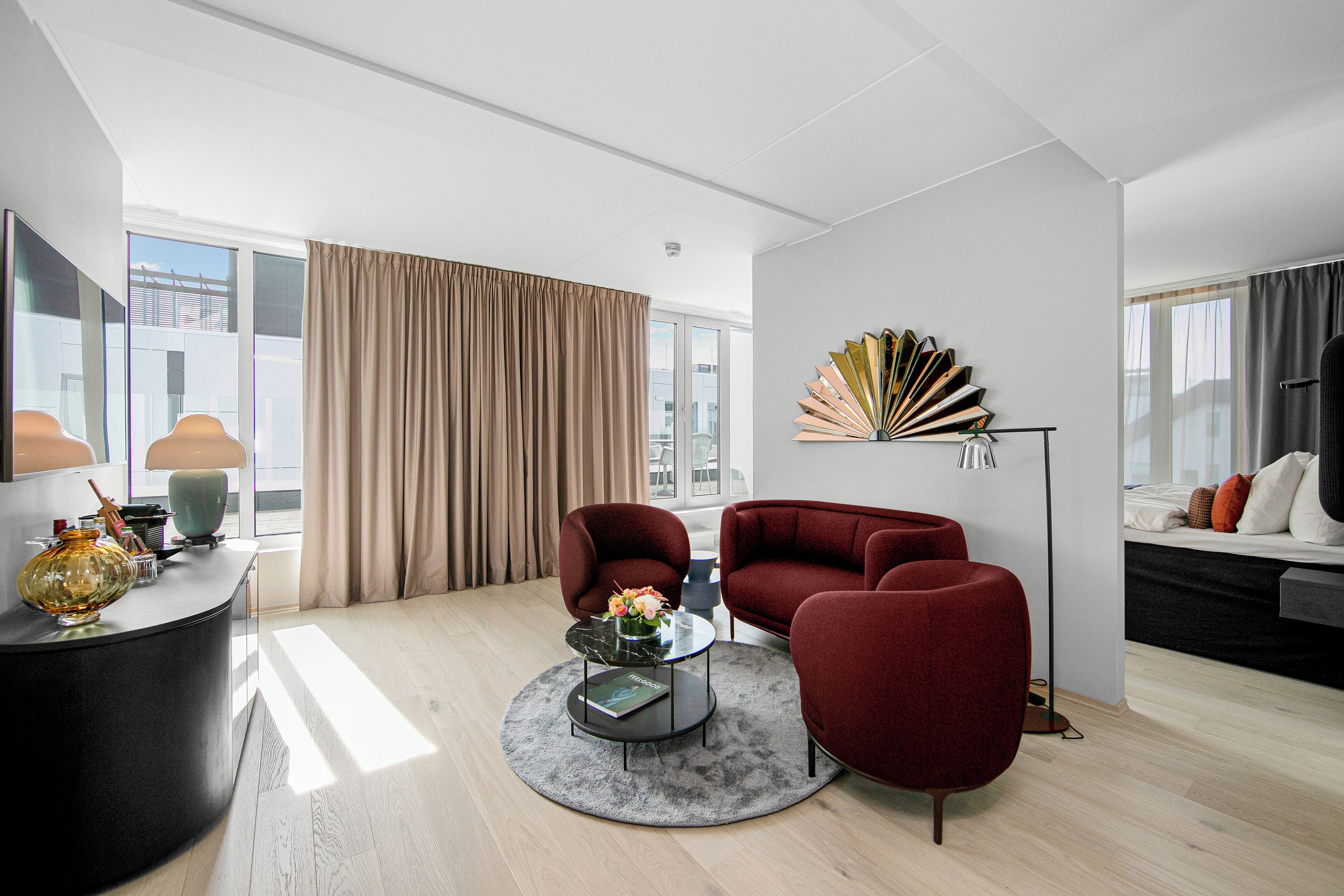 Un salon moderne avec une table basse ronde, deux fauteuils rouges, un canapé et un éventail décoratif accroché au mur.