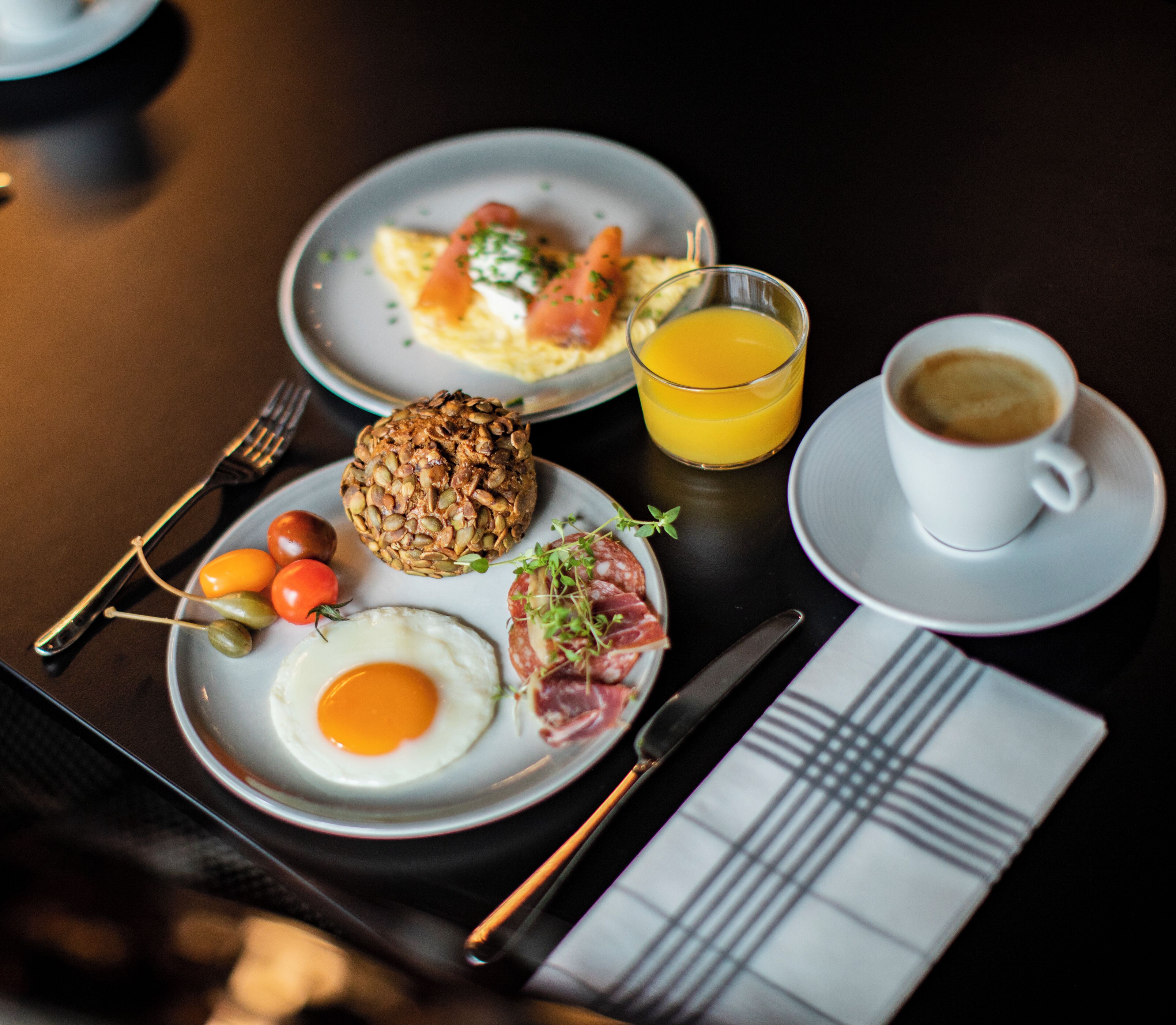 A breakfast setting with plates of food, a glass of orange juice, a cup of coffee, cutlery, and a napkin.