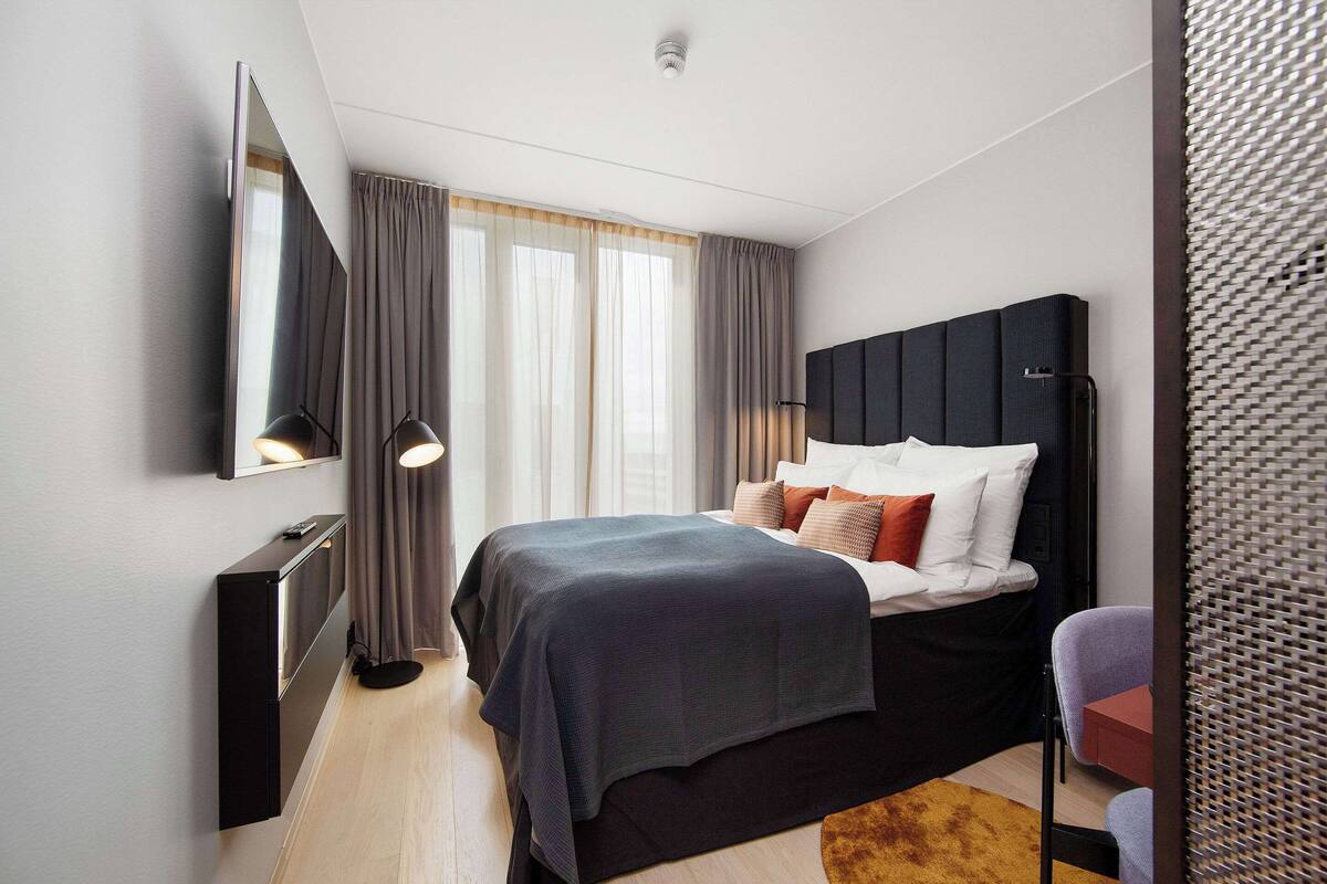 A modern hotel room with a bed, bedside table, and a large mirror.