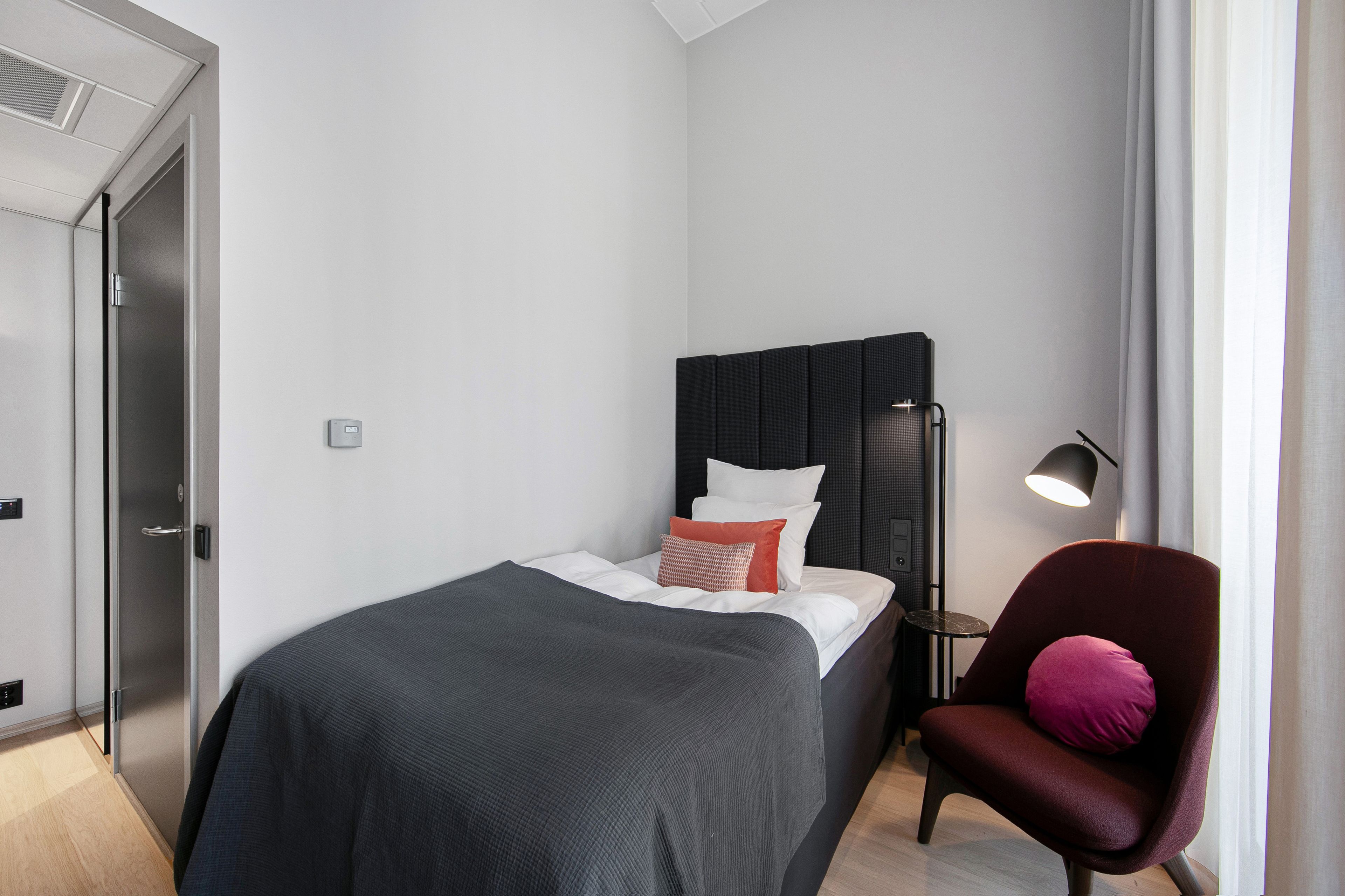 Et moderne hotelværelse med en seng, en stol, et sengebord og en lampe.