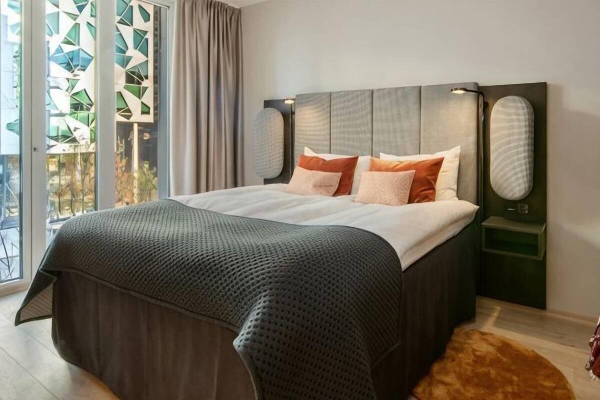 A bedroom with a large bed, a headboard with built-in speakers, and a view through a glass door.