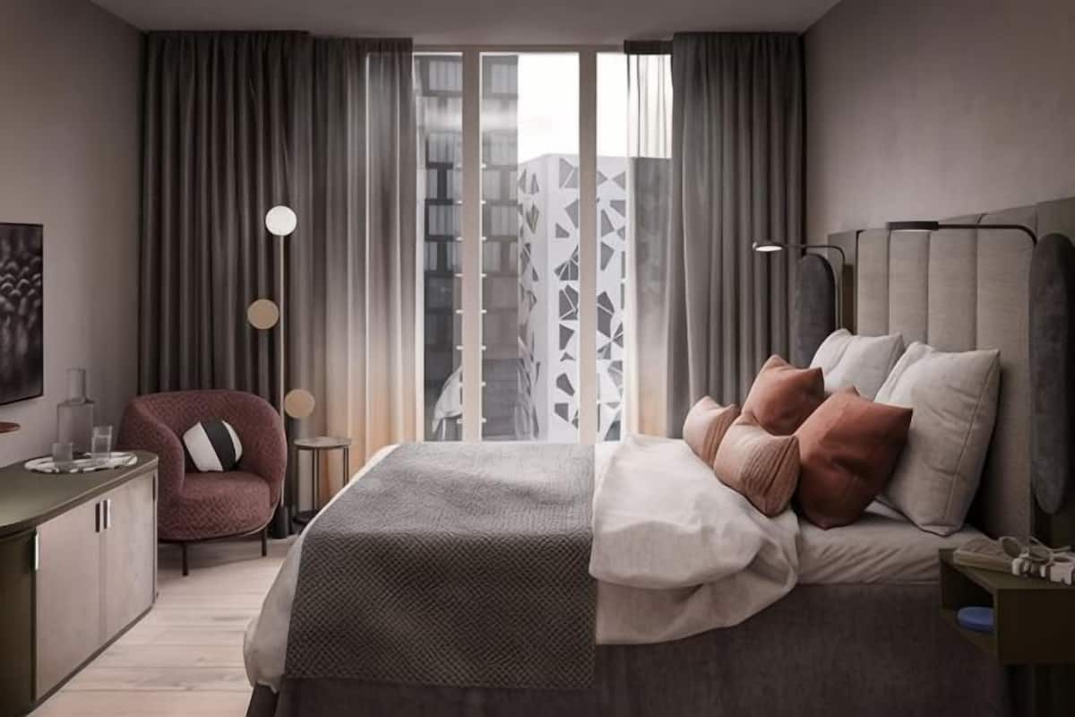 A modern hotel room with a bed, a desk, a chair, and a view of the city.
