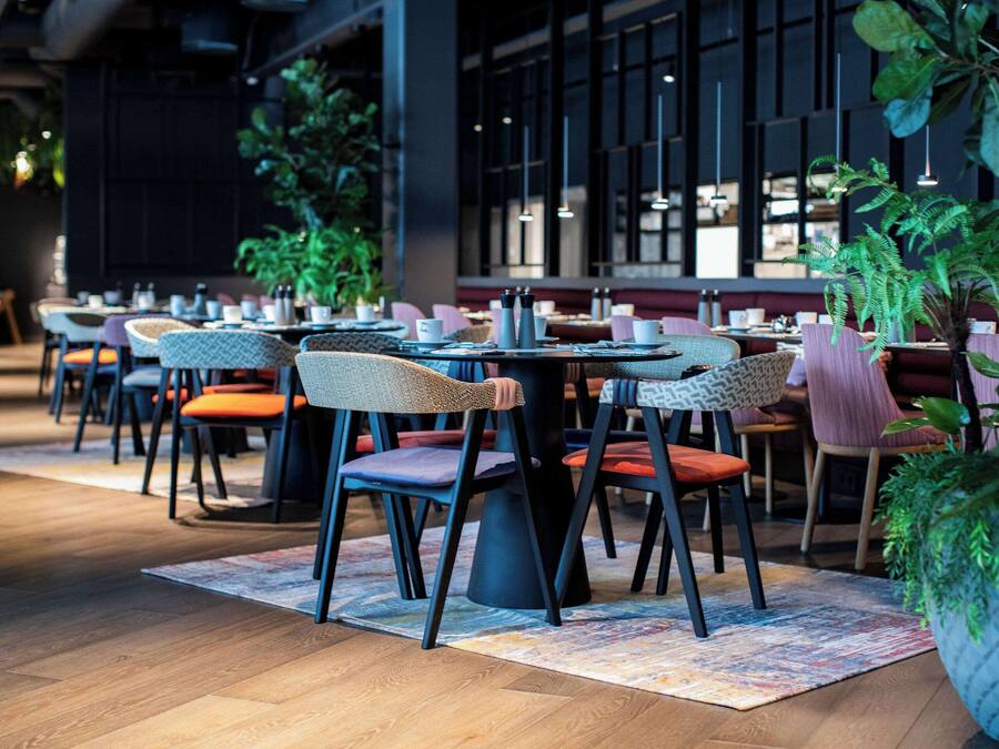 Ein modernes Restaurantinterieur mit runden Tischen, Korbstühlen und Topfpflanzen.
