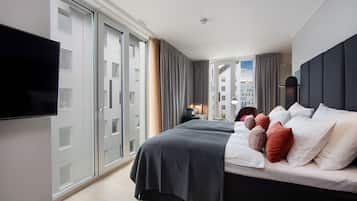 A modern hotel room with a large bed, a flat-screen TV, and a city view through the window.