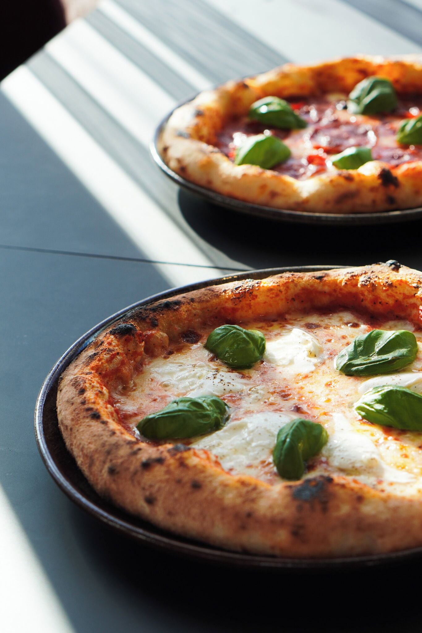Dos pizzas sobre una mesa con mantel a rayas.