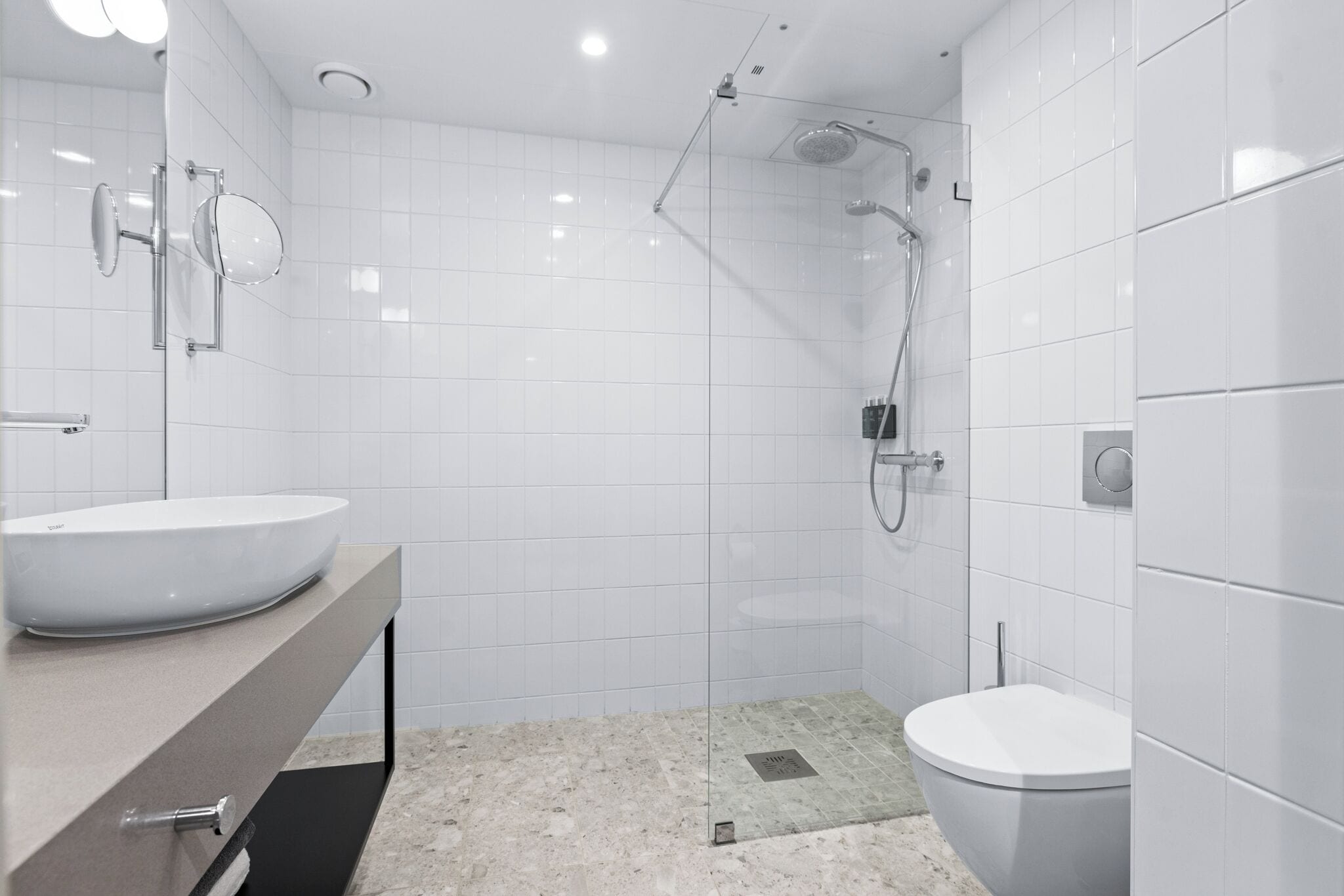 Un baño moderno con un lavamanos grande blanco, un inodoro y una zona de ducha con mampara de vidrio.