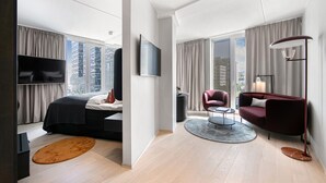 A modern hotel room with a large bed, a TV, a seating area with a sofa and armchair, and large windows offering city views. - Clarion Hotel Oslo (Oslo)