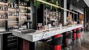 A modern bar with a marble countertop, black bar stools, and shelves stocked with liquor bottles and glasses. - Clarion Hotel Oslo (Oslo)