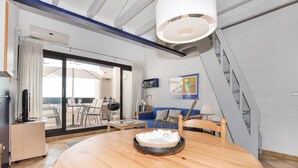 Een moderne woonkamer met een ronde houten tafel, een blauwe bank en een eethoek met een glazen tafel en stoelen.