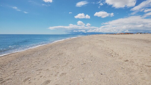 Een uitgestrekt zandstrand met een helderblauwe lucht en enkele wolken.
