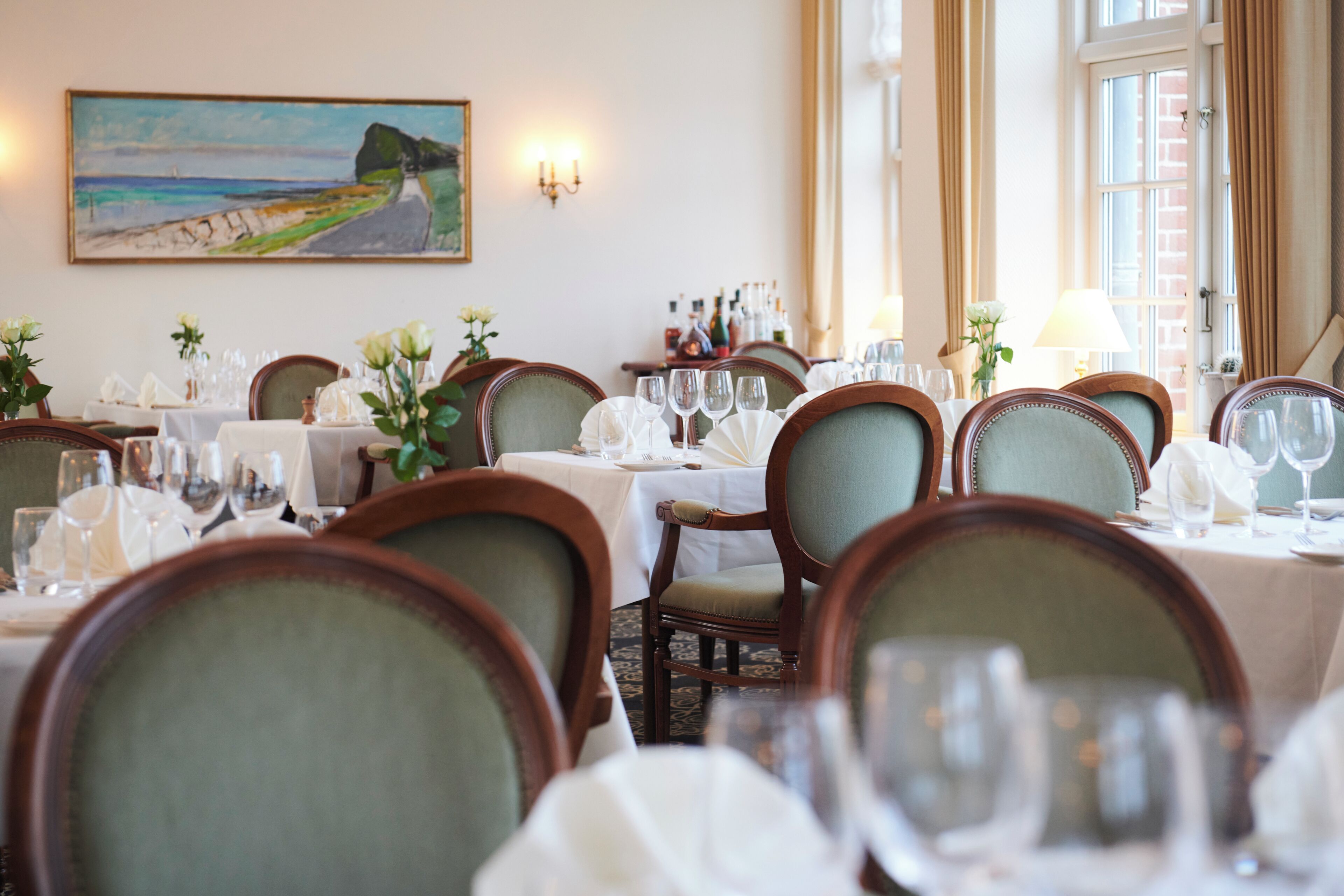 A dining area with multiple tables set for a meal, chairs, and a painting on the wall.