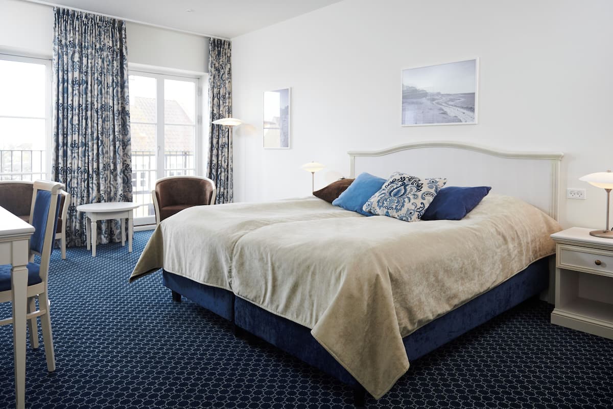 A hotel room with a large bed, a desk, a chair, and a window with curtains.