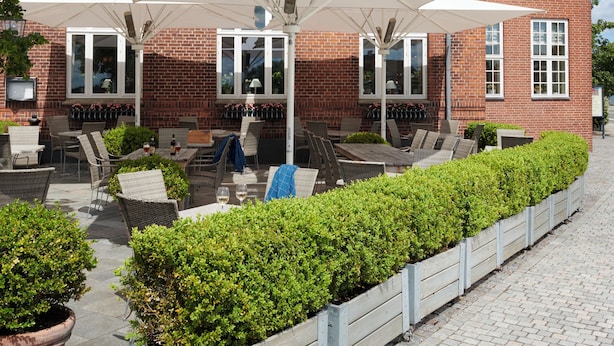 A brick building with a restaurant and hotel signage, outdoor seating with umbrellas, and a paved patio area. - Tornøes Hotel (Kerteminde)