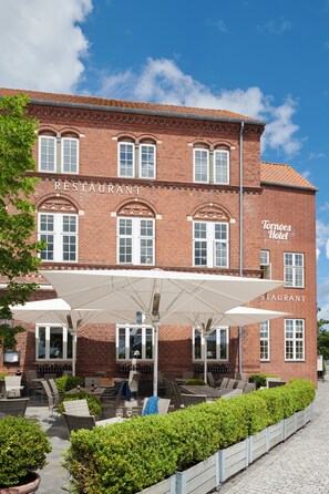 A brick building with a restaurant and hotel signage, outdoor seating with umbrellas, and a paved patio area. - Tornøes Hotel (Kerteminde)
