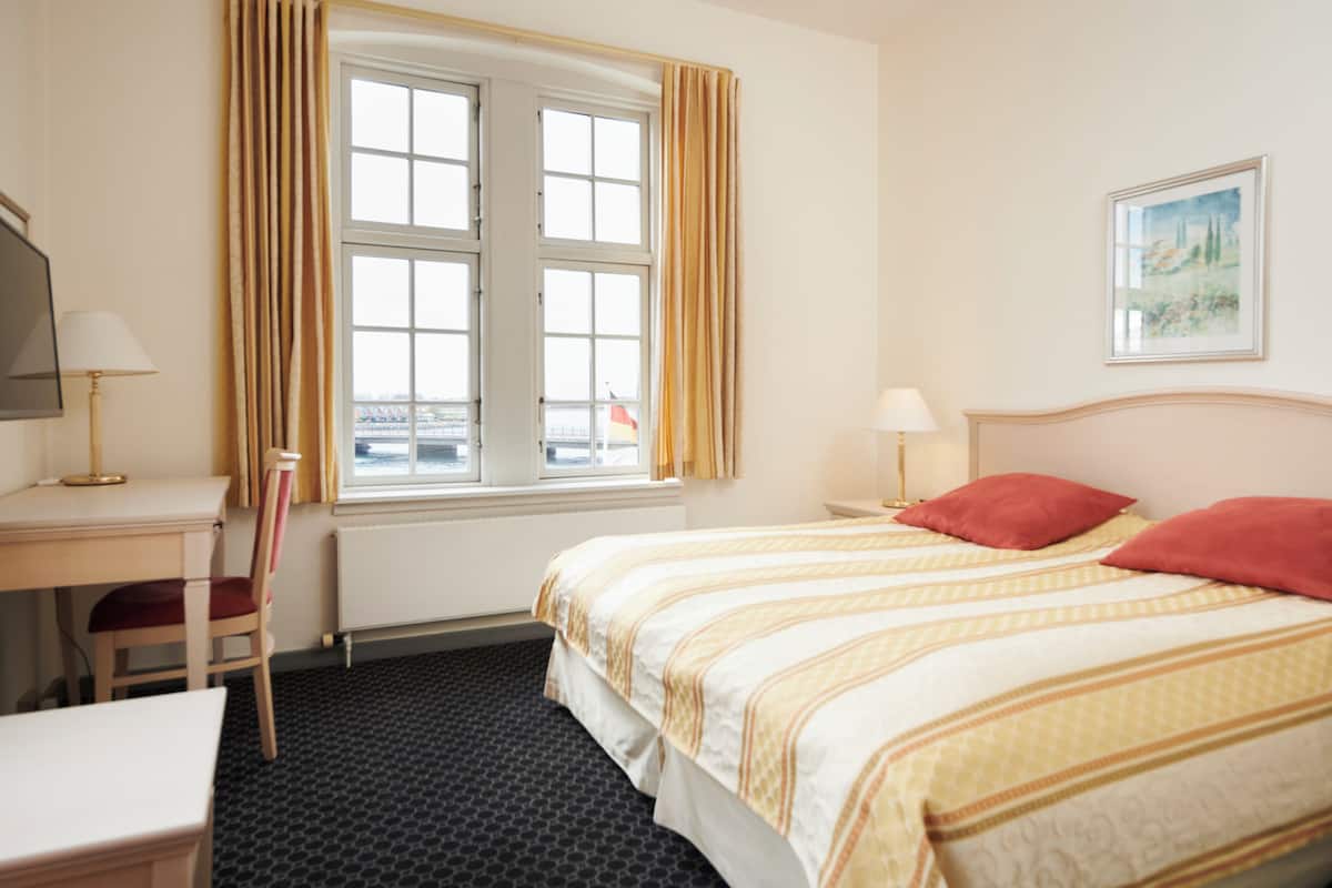 A hotel room with a bed, a desk, a chair, and a window with curtains.