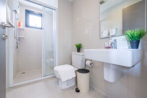 A modern bathroom with a glass shower enclosure, a toilet, a sink, and a potted plant.