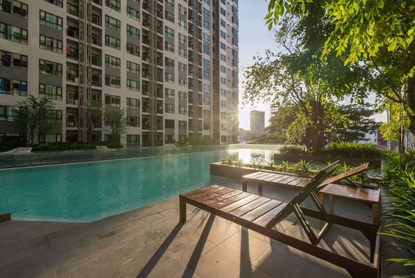 A modern hotel with a swimming pool, lounge chairs, and a view of high-rise buildings.