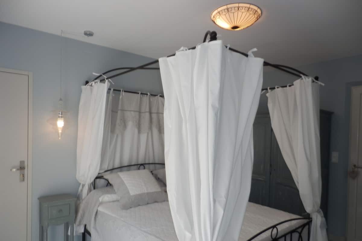 A bedroom with a four-poster bed, a bedside table, and a wall-mounted light fixture.