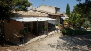 A house with a covered patio, a gravel driveway, and a garden with trees and shrubs. - Mas Les Vieux Chenes (Lambesc)
