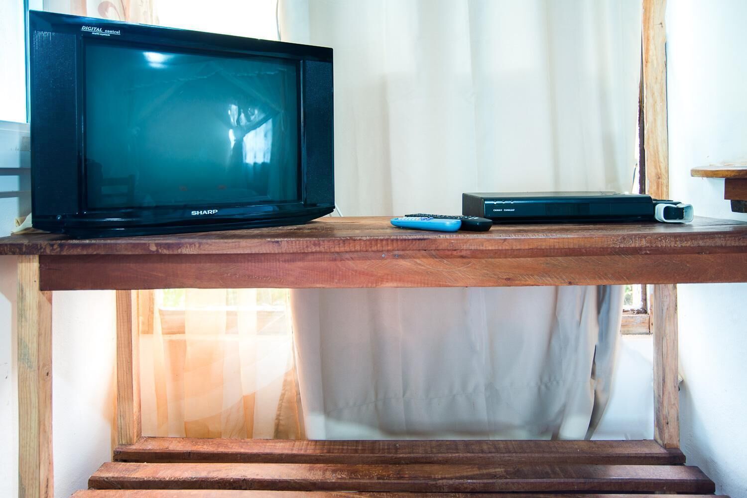 A television on a wooden shelf, a remote control, and a cable box.