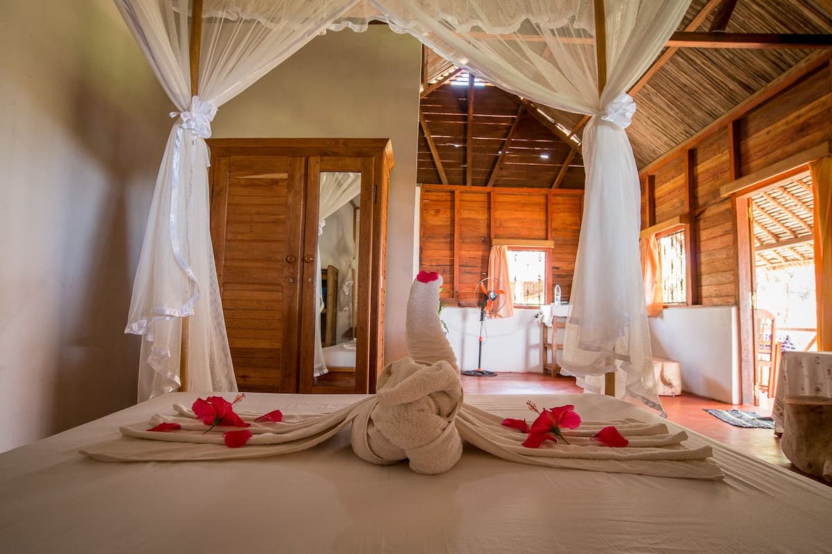Una habitación con una cama decorada con toallas y pétalos de rosa, paredes de madera y un ventilador de techo.