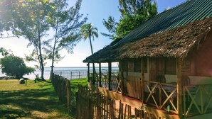 Una casa de madera con techo de paja, un muelle de madera y vista al mar.