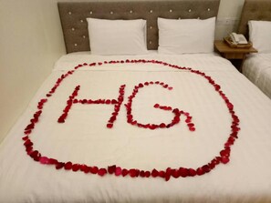 A bed with a white bedspread and pillows, a wooden nightstand with a telephone, and a headboard with a tufted design. - Hotel Grace Taunggyi (Taunggyi)