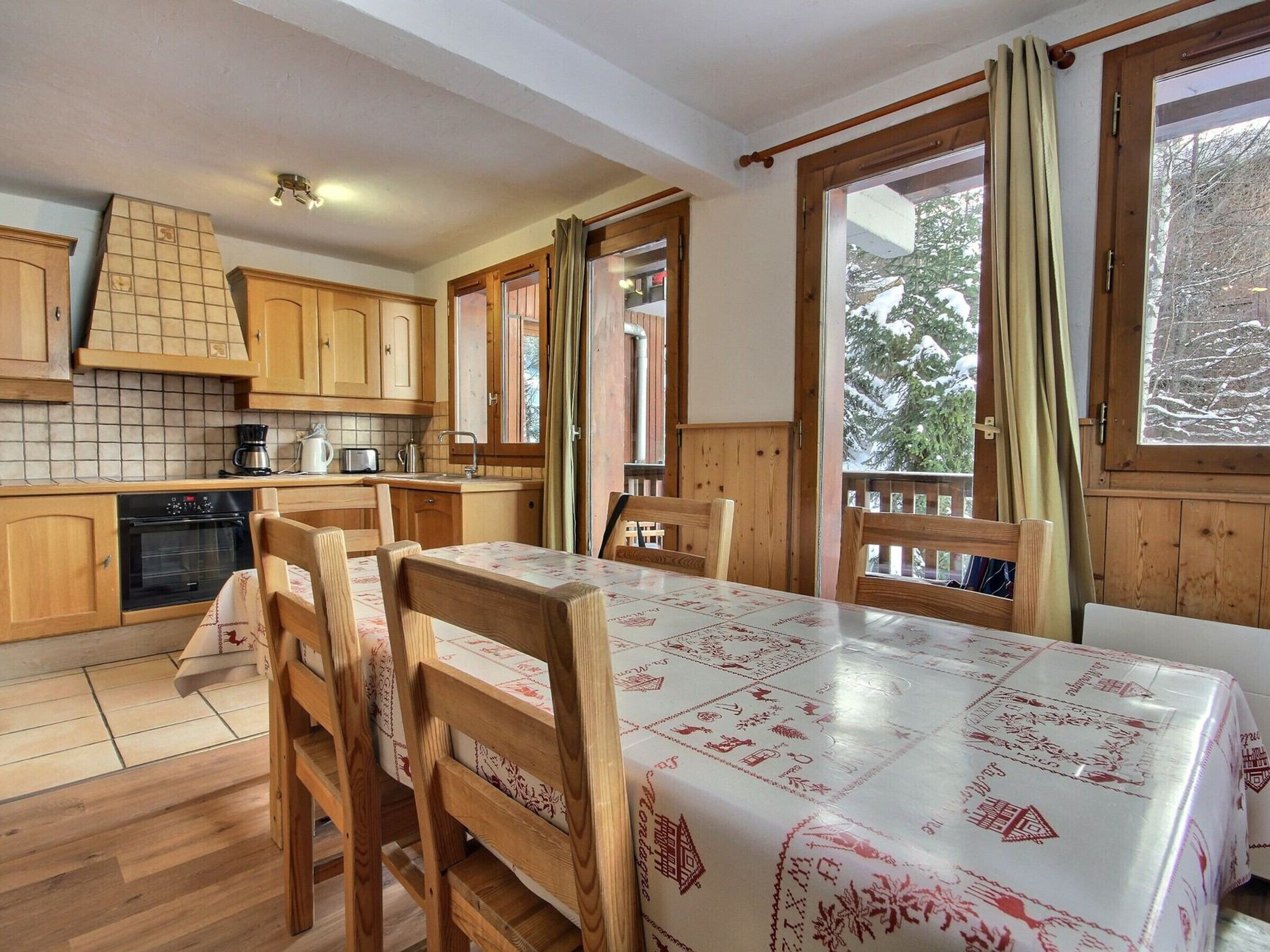Una cocina acogedora con armarios de madera, una mesa de comedor con sillas y ventanas amplias con cortinas.