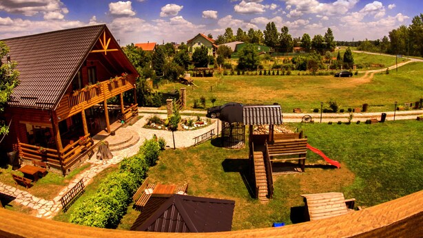 A wooden cabin with a porch, a barbecue area, and a fenced yard. - Bungalows Drevna (Novi Sad)