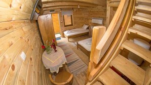 A wooden cabin interior with two beds, a small table with a vase, and a wooden chair. - Bungalows Drevna (Novi Sad)