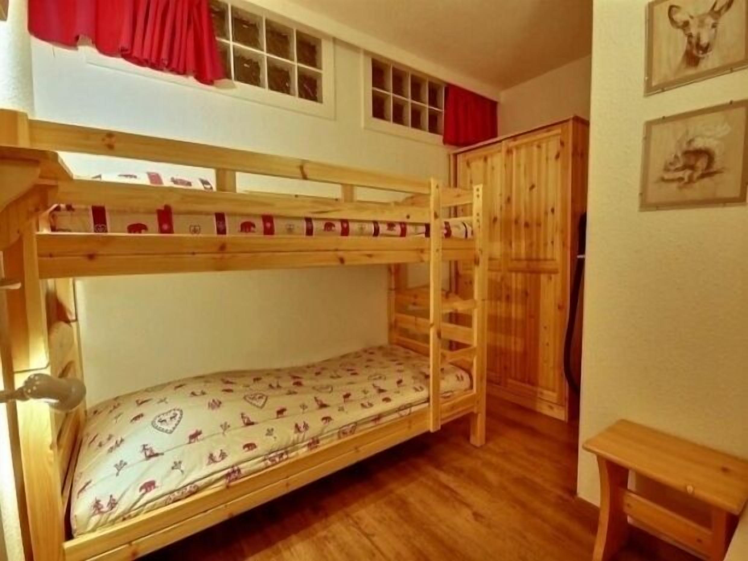 A bunk bed room with a wooden floor, a small desk, and a wardrobe.