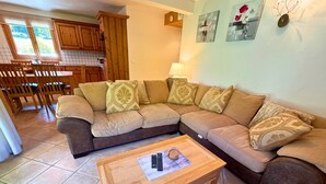 A living room with a sectional sofa, a wooden coffee table, and a kitchen in the background. - Spacious 4-Room Apartment with Ski Access, Balcony, and Stunning Views near Les Menuires (Saint-Martin-de-Belleville-Les Menuires)