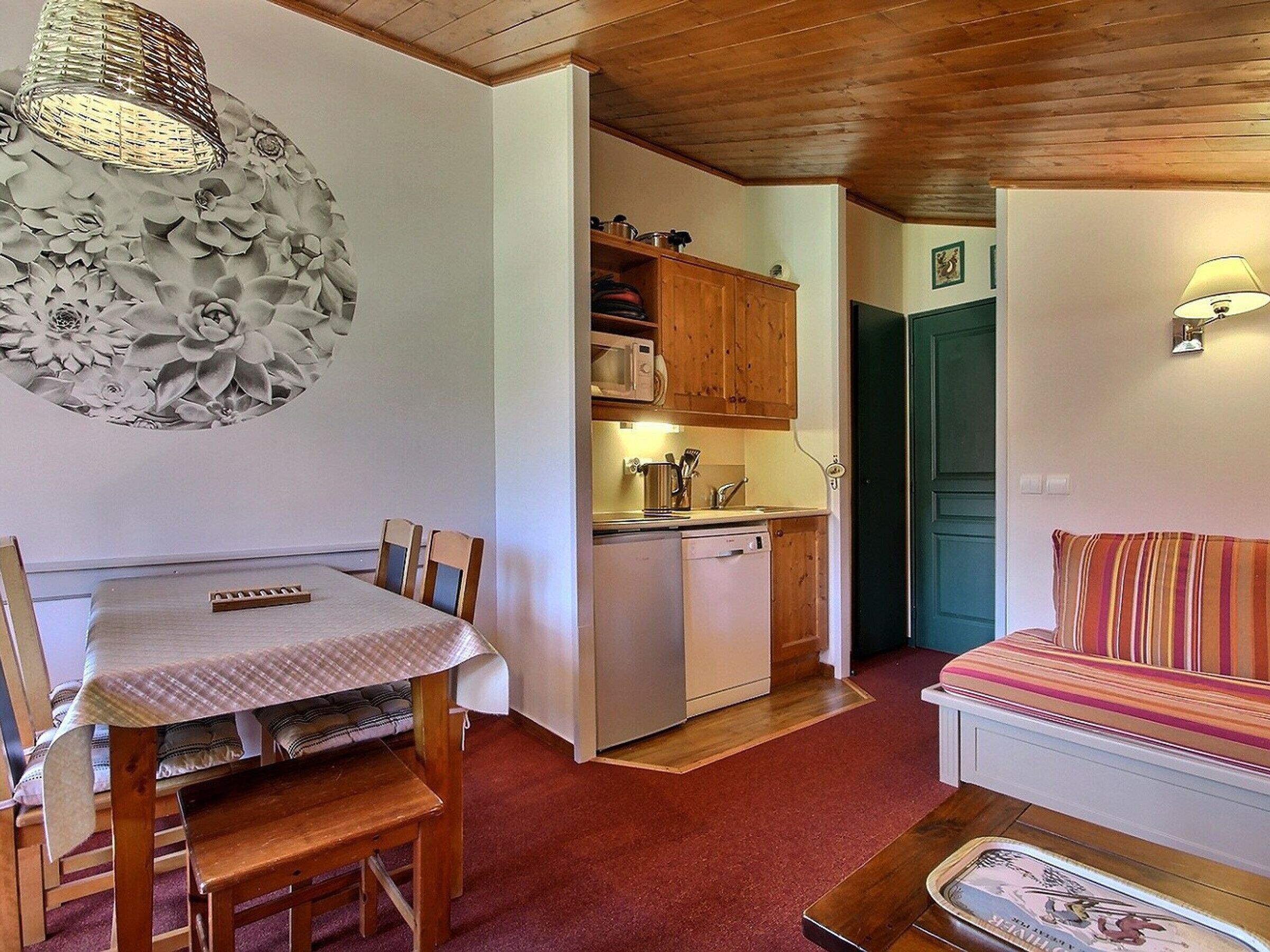 A compact living space with a dining table, chairs, a sofa, a kitchenette, and a decorative wall piece.