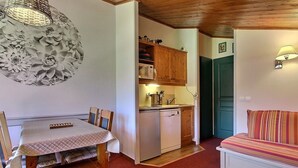 A compact living space with a dining table, chairs, a sofa, a kitchenette, and a decorative wall piece. - South-facing apartment at slopes, 5 people, balcony (Plagne Soleil)