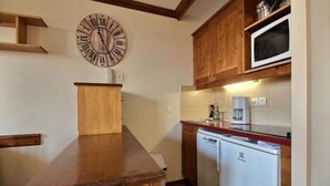 Eine kleine Küche mit Holzausbau, einer eingebauten Mikrowelle und einer Wanduhr.