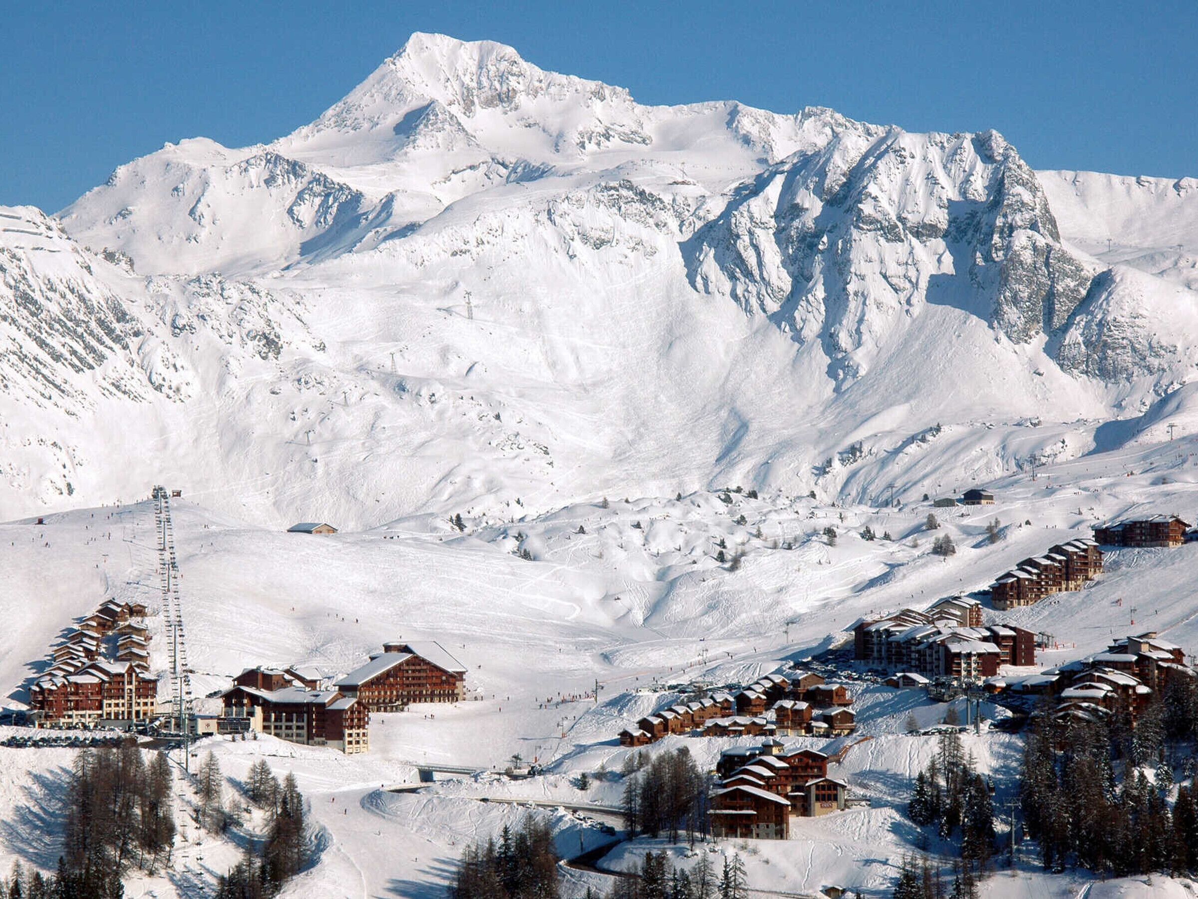 A snow-covered mountain with a ski resort, including lodges and a ski lift.