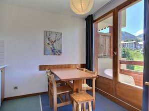 A room with a wooden table and chairs, a painting of a deer, and a view of mountains through a large window.