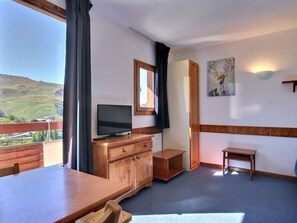Una habitación con un tocador de madera, un televisor, una mesita pequeña y un cuadro en la pared.