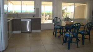 Una cocina con lavavajillas, una mesa de comedor con sillas y vistas al océano a través de amplios ventanales.