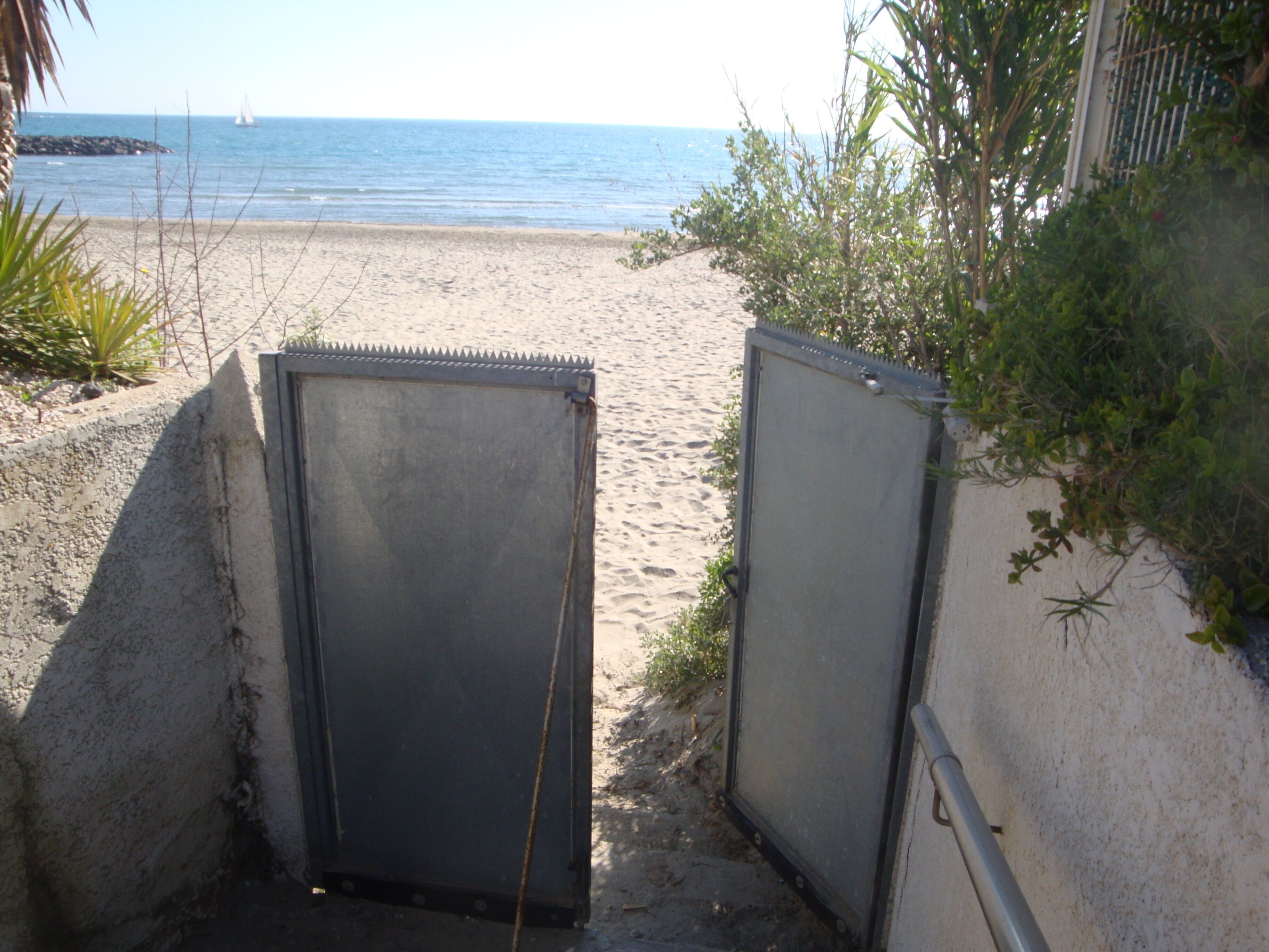 Een toegang tot het strand met metalen deuren die uitkomen op een zandgebied.