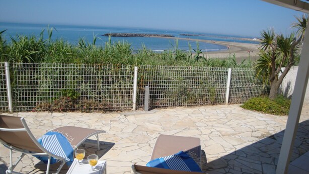 Un patio con dos sillones, una mesa y vistas a la playa y al océano.