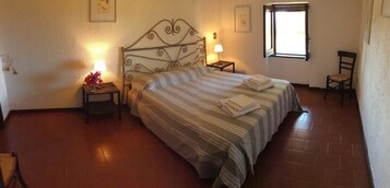 Un dormitorio con una cama, dos mesitas de noche, una silla, una ventana y un cuadro colgado en la pared.
