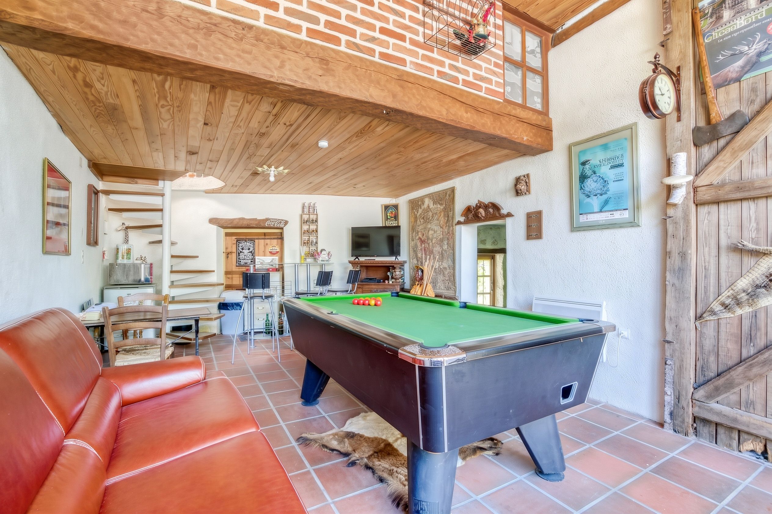 Una mesa de billar en una habitación con pared de ladrillo, techo de madera y mesa de billar.