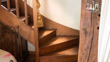 A wooden staircase with a rope handrail, a white wall, and a rustic chandelier.