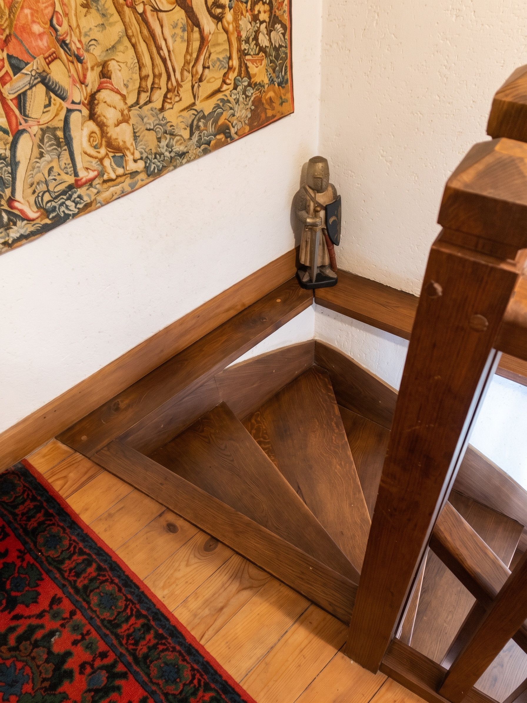 A wooden staircase with a decorative rug and a statue.