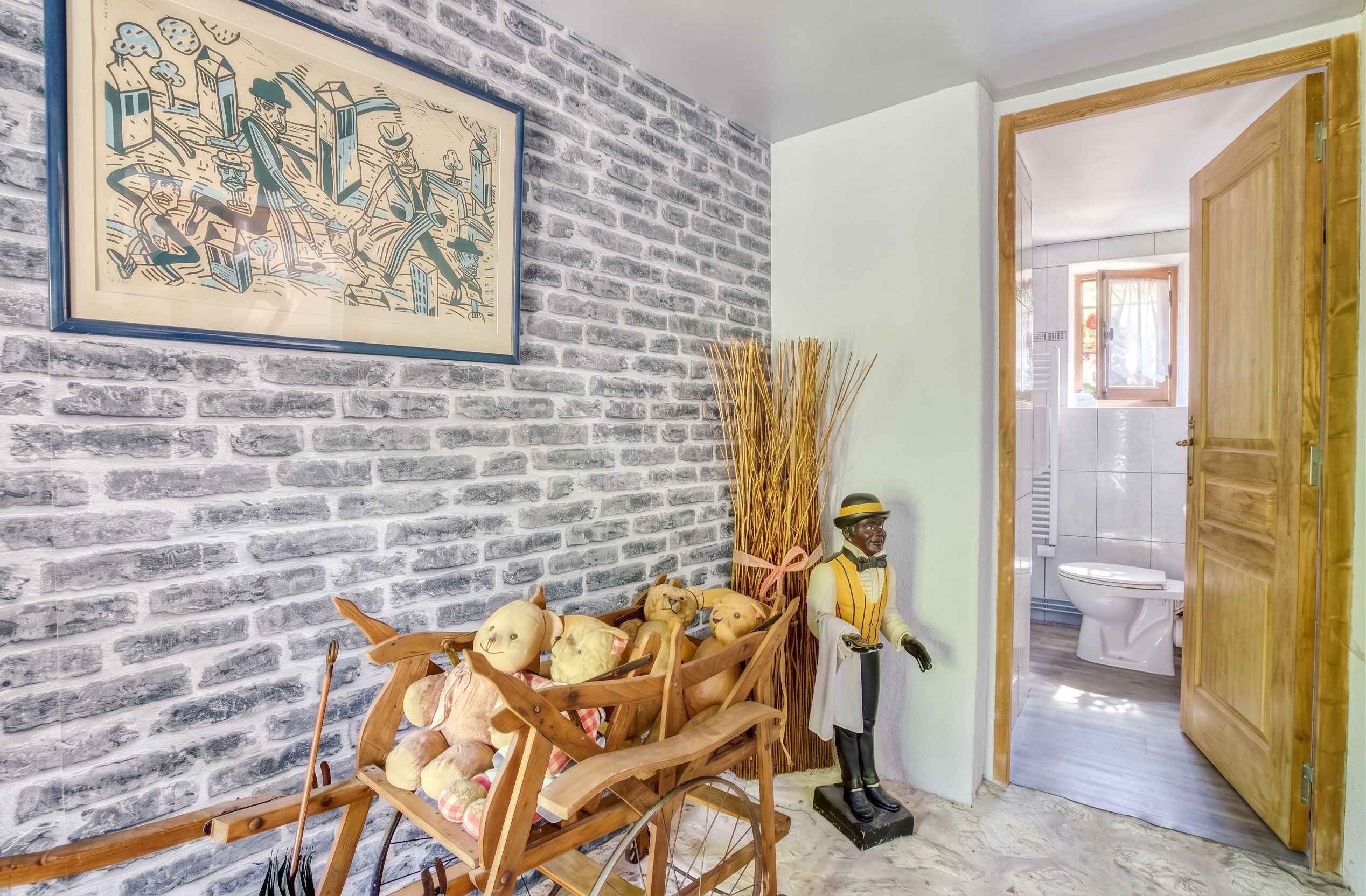 Une pièce avec un mur en briques, un chariot en bois rempli de peluches, une figurine et un tableau encadré.